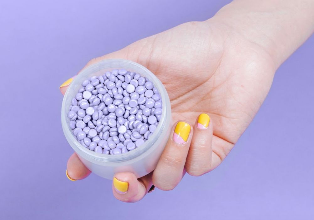 A hand holding wax melts in a jar