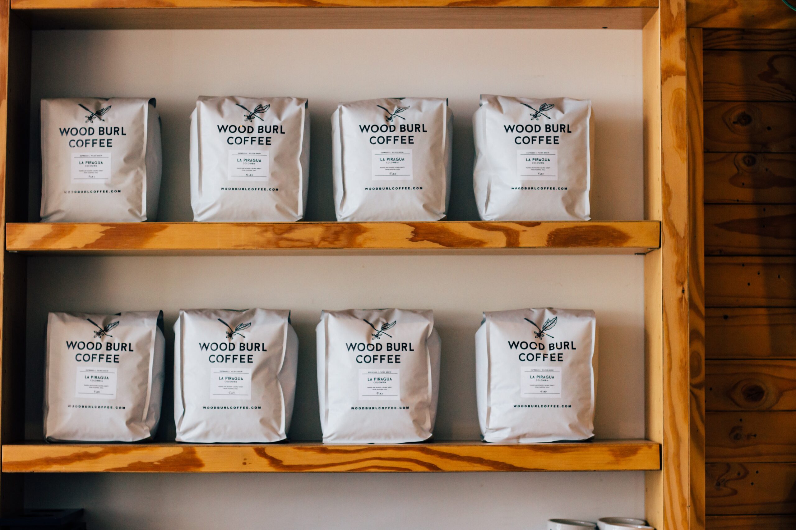 Eight coffee bags on a wooden shelf.