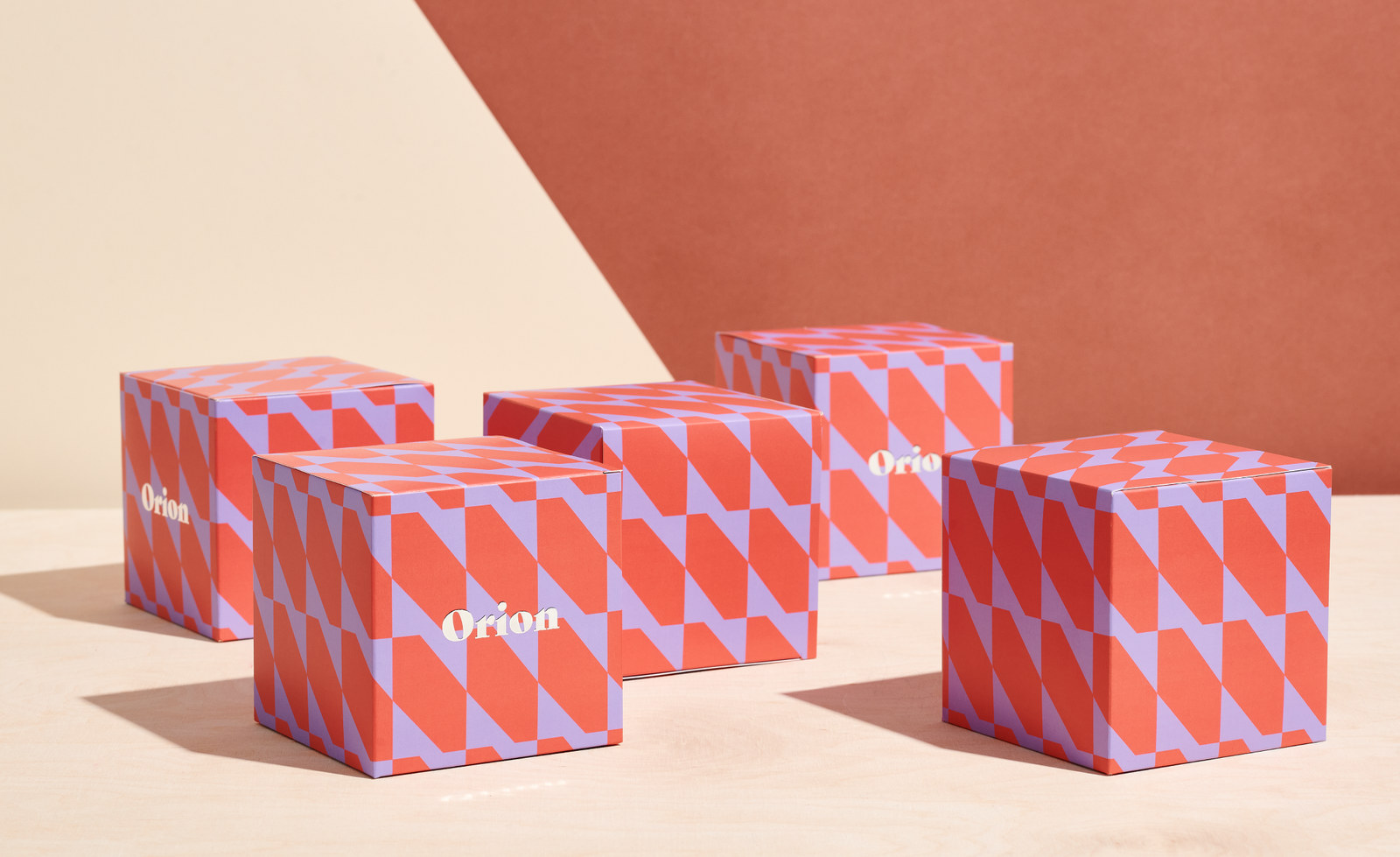 Colorful packaging boxes with a red and lavender geometric pattern displayed on a light wooden surface